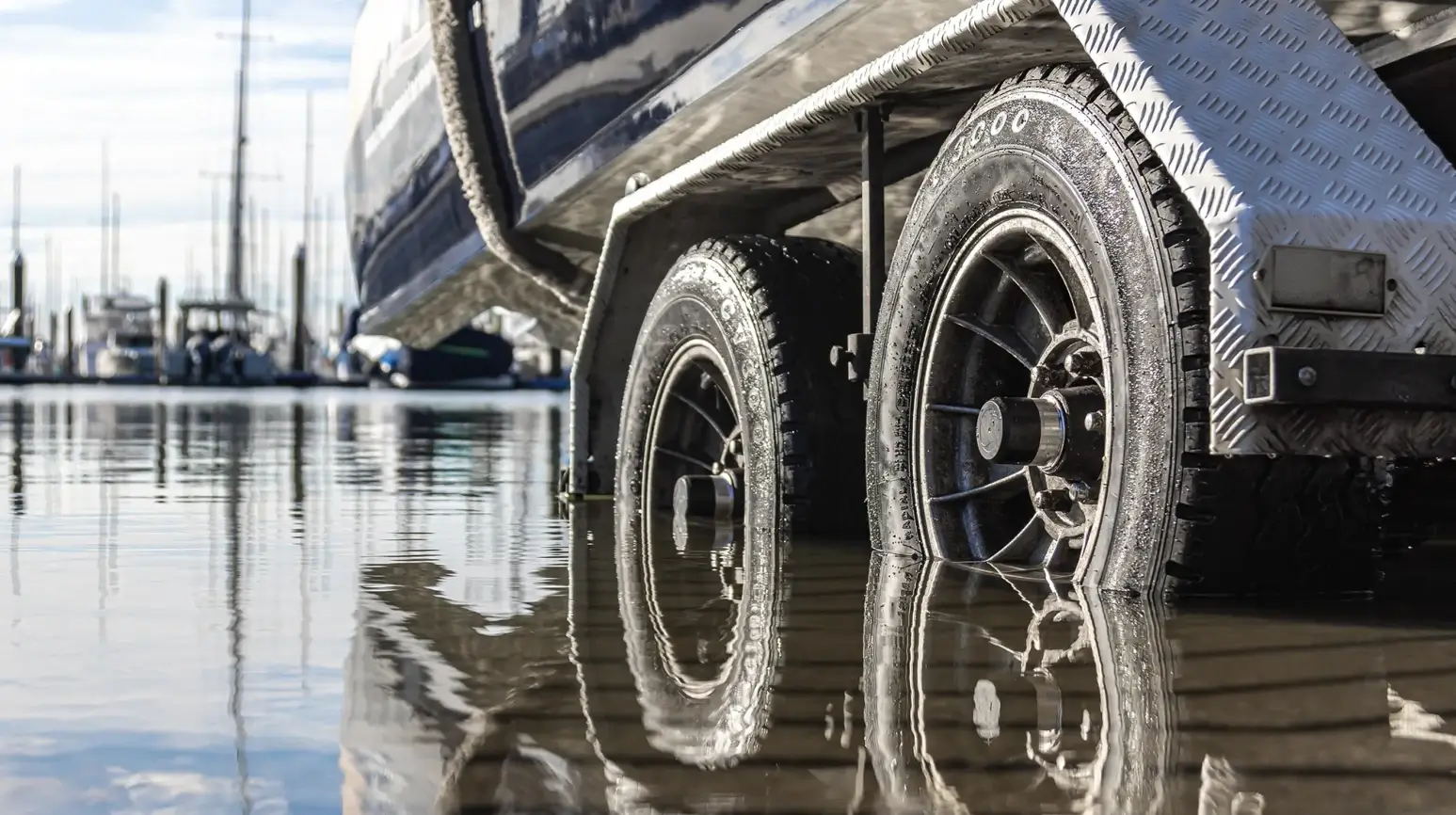 Towing a boat safely with Wheel Sensei: Close-up of boat trailer wheels submerged in water during launch, showing hub and bearing exposure to saltwater moisture.
