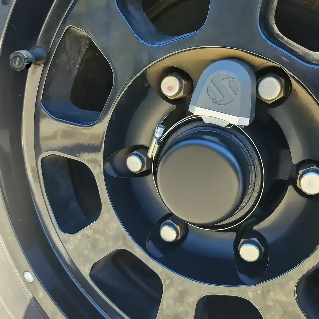 Close-up of a Wheel Sensei Trailer Monitoring System bearing sensor mounted on a black alloy wheel hub, showing the smart temperature and bearing monitoring system by Smarter Towing.
