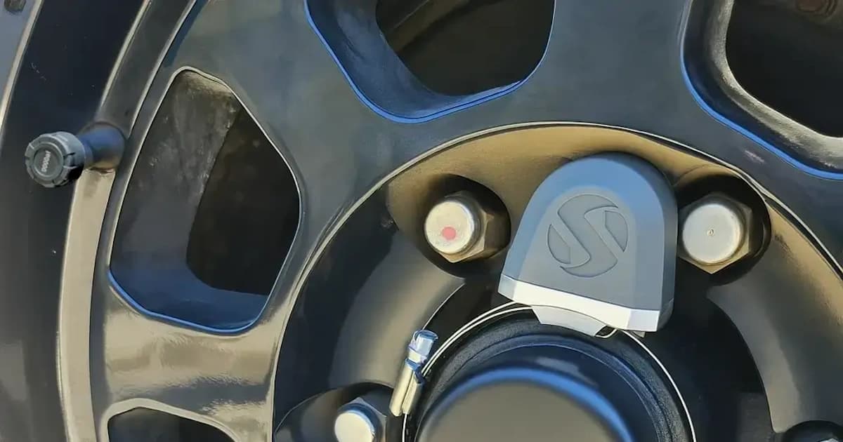 Close-up of a Wheel Sensei bearing temperature sensor mounted on a black alloy wheel hub, showing the smart temperature and bearing monitoring system by Smarter Towing.